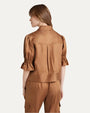 The backside knee-up view of a brunette model wearing a brown jacket with a collar and bunching at the elbows. She is also wearing matching brown pants and is standing in front of a plain white background.