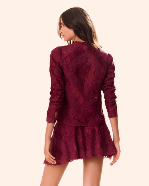 A knee-up backside view of a brunette model with her hair swept to the side wearing a long-sleeved maroon blouse with intricate floral and geometric patterns. The shirt is paired with a matching skirt, and the model is standing in front of a white background.