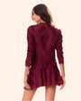 A knee-up backside view of a brunette model with her hair swept to the side wearing a long-sleeved maroon blouse with intricate floral and geometric patterns. The shirt is paired with a matching skirt, and the model is standing in front of a white background.