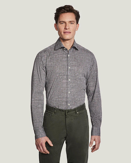 A knee-up view of a model wearing a grey button up shirt tucked into green buttoned pants, standing in front of a white background.
