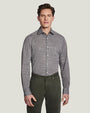 A knee-up view of a model wearing a grey button up shirt tucked into green buttoned pants, standing in front of a white background.