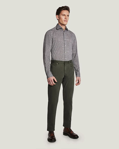 An angled full body view of a model wearing a grey button up shirt tucked into green buttoned pants and white sneakers, standing in front of a white background.
