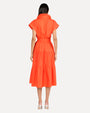 The backside view of a person wearing an orange dress with short, rolled sleeves and a collar. The dress has a tied fabric belt at the waist and falls to mid-calf length. The model is standing against a white background.