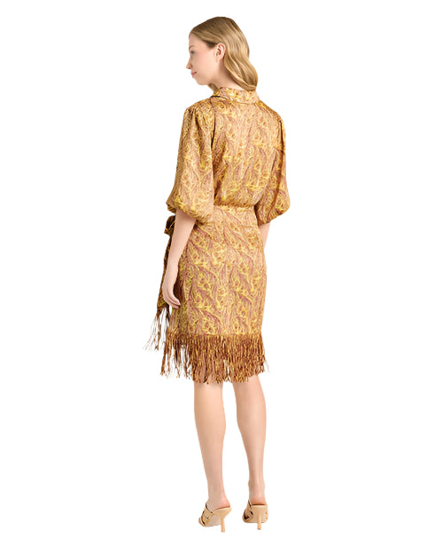 Back view of a person wearing a knee-length dress with a yellow and brown intricate pattern, short sleeves, a belted waist, and fringe detailing at the hem, paired with beige heeled sandals.