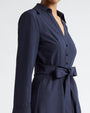 A close-up side view of a model wearing a navy long-sleeved button-down dress with a V-neck and a tied fabric bow at the waist.