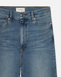 A close-up waist level view of a pair of blue jeans with a slightly faded and worn-in look. The jeans feature a button and zipper closure, and a white tag reading "FRAME" on the inner waistband.