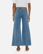 A backside, lower body shot of a model wearing blue wide-leg jeans with a brown belt. The denim has a slightly faded and worn-in look and is paired with a tucked in white shirt and brown slides. The model is standing in front of a white background.
