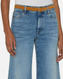 A close-up waist-level view of a model with her hands by her sides, wearing blue wide-leg jeans with a high waist and a brown belt.