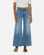 A lower body shot of a model wearing blue wide-leg jeans with a brown belt. The denim has a slightly faded and worn-in look and is paired with a tucked in white shirt and brown slides.