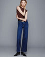 A full body shot of a model standing against a plain gray background wearing a sleeveless brown top tucked into high-rise blue jeans with a straight-leg cut and a black belt with a gold buckle, and black pointed-toe ankle boots with a low heel.