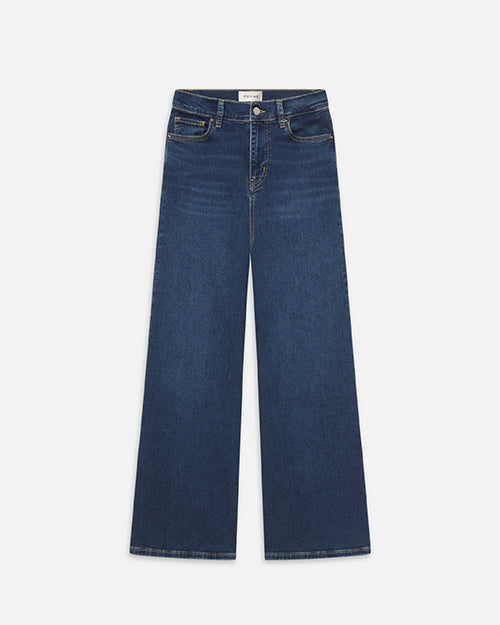 A pair of wide leg blue jeans with a white rectangular tag on the inner waistband. The background is white.