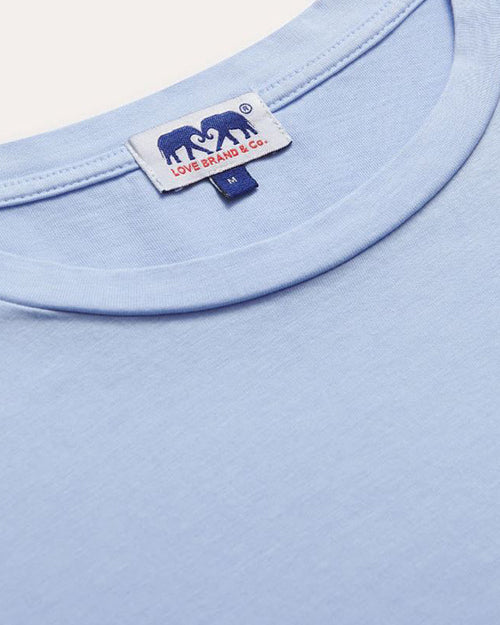 A close-up of the neckline of a blue crewneck T-shirt with a white rectangular tag showcasing two elephants and the brand name "LOVE BRAND & CO.", and "M".