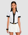 A person wearing a white short-sleeved top with black accents on the collar, button line, and sleeve edges, featuring gold buttons. They are also wearing a white pleated skirt with a black belt and gold buckle, and gold accessories