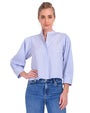A blonde model standing against a white background is wearing a light blue and white thin striped blouse with long sleeves, a mandarin collar, and a hidden button-down design. The model is also wearing blue jeans and silver hoops.