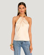 A knee up view of a brunette model wearing a light beige strapless halter top with a pleated design at the neckline, connected to a colorful oval beaded necklace paired with high-waisted blue jeans. The model is also wearing a chunky bracelet and is placed behind a blank background.