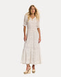 Front view of a woman wearing a white lace dress  with wedges against a plain background