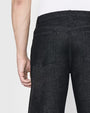 A backside waist level view of a model wearing black jeans tucked into a white shirt. The background is plain white.