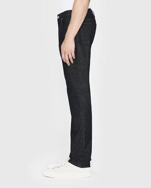 A lower body sideview of a model wearing black jeans tucked into a white t-shirt and sneakers. The background is completely white.
