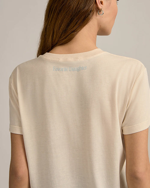 A close-up backside view of a brunette model with her hair swept to the side, wearing silver hoop earrings and a beige crewneck t-shirt with the words "Favorite Daughter" in light blue below the neckline.
