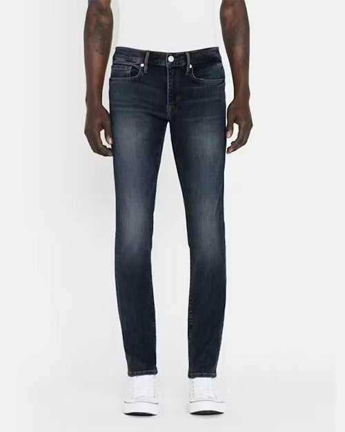 A lower body view of a model wearing a white shirt tucked into a pair of dark blue jeans with a faded wash, and white sneakers. The mode is standing in front of a white background.