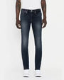 A lower body view of a model wearing a white shirt tucked into a pair of dark blue jeans with a faded wash, and white sneakers. The mode is standing in front of a white background.