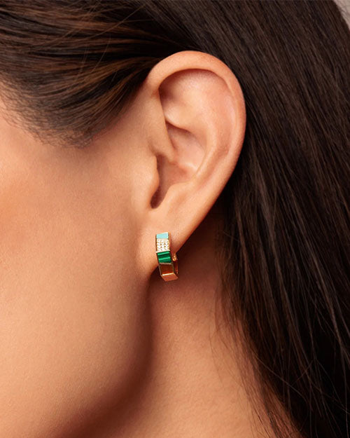 A close-up image of a brunette models' ear showcasing a hexagonal gold hoop earring with a multi-color design and a gold outline.