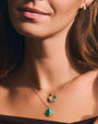 A close-up view of a models' neck wearing two necklaces and an earring, all multi-colored with gold outlines. One pendant is a horseshoe, and one is a peace sign.