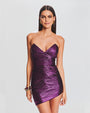 A knee-up view of a brunette model wearing a strapless, shiny purple dress with ruched detailing all across it and a sweetheart neckline. The model is also wearing multiple gold bangles, gold earrings, and is standing in front of a white background.