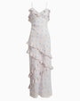A full image of a long, sleeveless dress with thin straps. The dress is white with a subtle blue floral pattern and features ruffles along the neckline, across the front leg area, and at the hem.