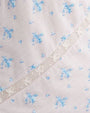 A close-up of a dress's white fabric with a small blue floral pattern. There is also a strip of lace running diagonally across the fabric with a delicate, intricate design.