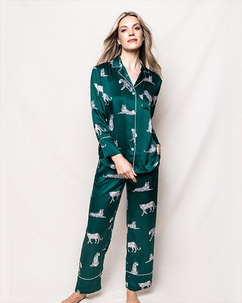 A full body image of a blonde model wearing a matching green long-sleeved button-down pajama set with leopards all over it. The model is standing in front of a white background.