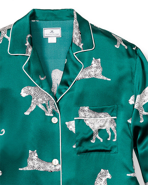 Close up of an emerald, green button-down pajama shirt with a chest pocket, and a white leopard cat pattern. There is a rectangular white tag in the inner neckline. The background is white.