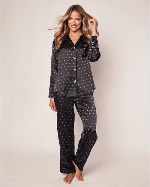 A full-body view of a blonde model wearing a matching black and white polka-dot pajama set consisting of a button-down shirt and pants. The background is plain white.
