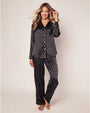 A full-body view of a blonde model wearing a matching black and white polka-dot pajama set consisting of a button-down shirt and pants. The background is plain white.