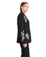 Side view of a woman wearing a black outfit with white floral embroidery on a white background