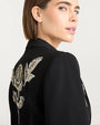 Close up of a back view of a person wearing a black jacket with intricate metallic floral embroidery, including roses, accented with beads or sequins.