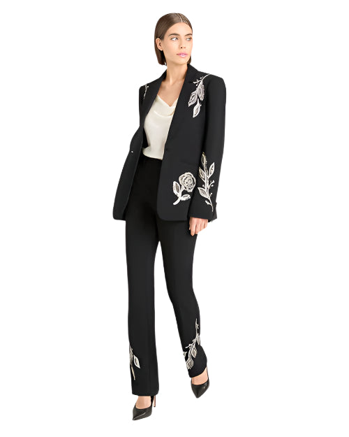 Woman wearing a black suit with white floral embroidery with black heels on a white background