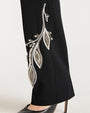Close up of a black pants with silver leaf embroidery on a white background
