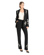 Person wearing a black pantsuit with white floral embroidery on the blazer and pants, paired with a white blouse and black high-heeled shoes