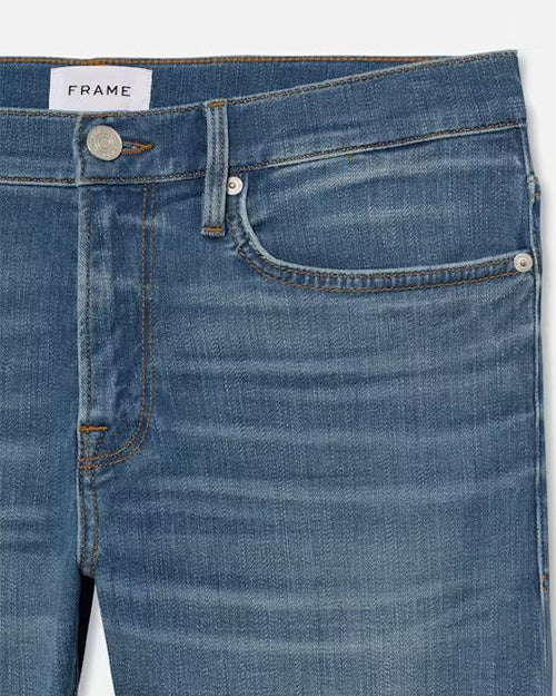 A close-up hip-level blue jeans with a faded wash at the knees and a white rectangular tag in the inner waistline. The background is plain white.