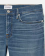 A close-up hip-level blue jeans with a faded wash at the knees and a white rectangular tag in the inner waistline. The background is plain white.