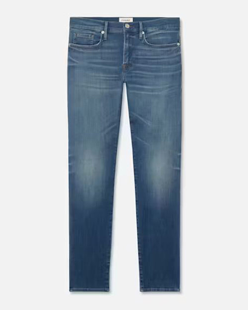 A pair of blue jeans with a faded wash at the knees and a white rectangular tag in the inner waistline. The background is plain white.