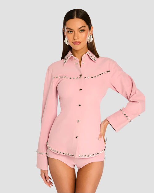 A woman modeling a primrose pink suede shirt with snap button cuffs and silver-tone studded detailing on a light color background.