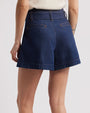 A close waist-level view of a model wearing a white shirt tucked into a pair of high-waisted, dark blue denim shorts with an attached denim belt. The background is white.