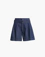 A pair of dark blue denim shorts with pleats, and an attached denim belt featuring a vertical rectangular buckle. The shorts are placed in front of a white background.