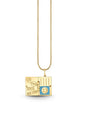 A gold chain necklace with an open-book shaped pendant featuring travel-themed designs. The pendant includes stickers labeled 'PARIS,' 'TOKYO,' and 'NEW YORK,' along with a small blue square with a smiley face in the bottom right corner. The necklace is draped against a white background.