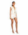 A complete image of a person wearing a sleeveless white vest with beige trim and gold buttons. There are two chest pockets and two hip pockets with button closures. The model is accessorizing with two white bracelets on and high heels.