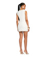 The backside view of a person wearing a sleeveless white vest with beige trim. The model is accessorizing with two white bracelets and white high heels.