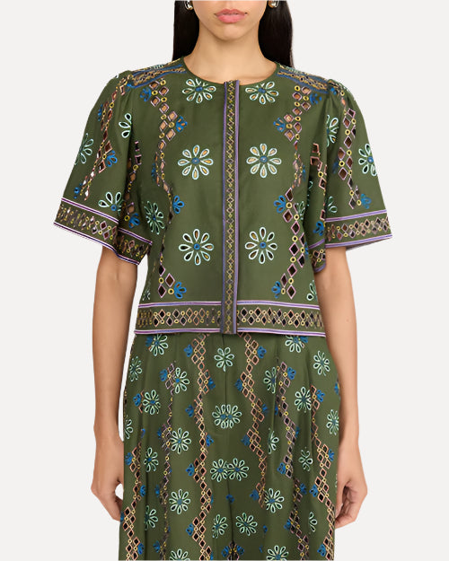 A zoomed in frontal view of a dark-haired model standing against a white background and wearing a matching green short-sleeved top and bottoms with intricate patterns including floral and geometric designs.