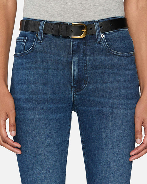 A close-up waist level view of a model wearing a grey shirt tucked into a pair of blue denim jeans with a black belt. The denim has a slightly worn and faded look around the thighs.